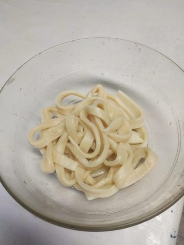 Des nouilles udon cuites et disposées dans une assiette translucide