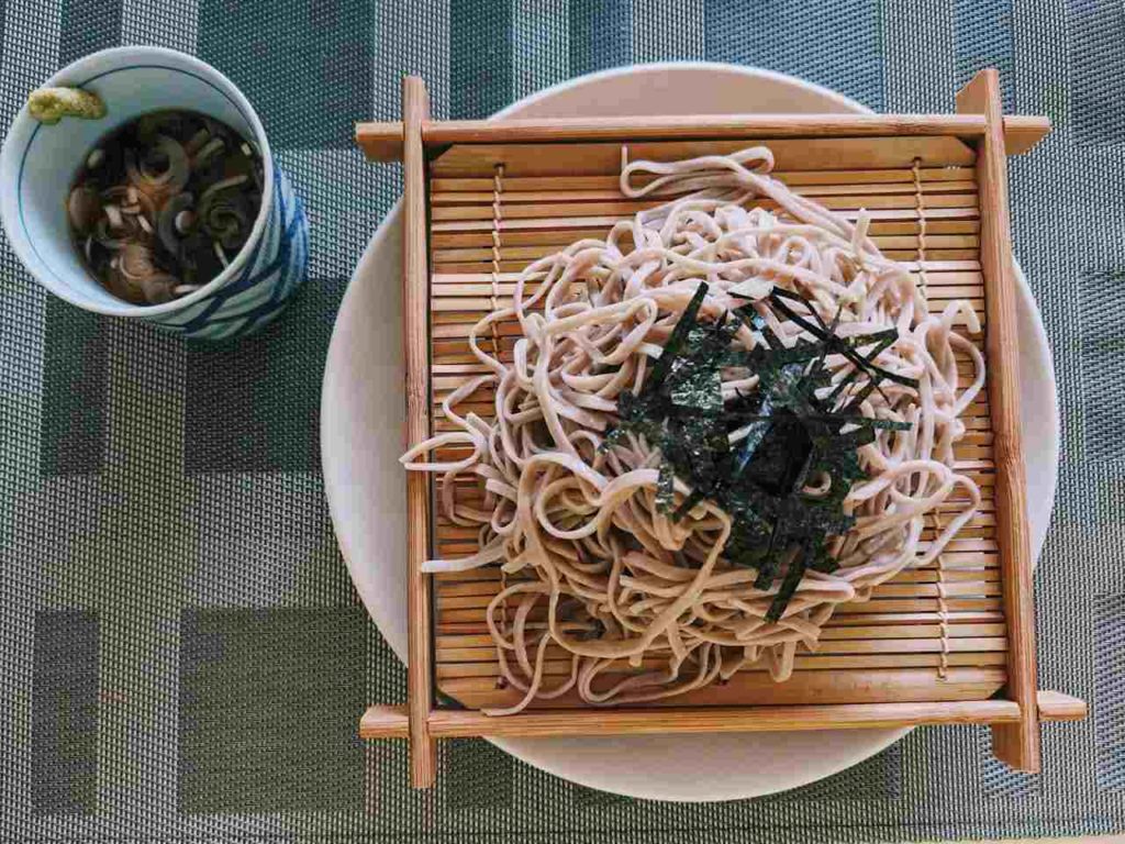 un plateau en bambou sur lequel sont déposées des nouilles soba pour composer un plat de zaru soba