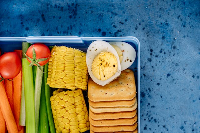 Un bento ou boite à repas japonaise qui contient du maïs, des tucs, des oeufs durs, des batonnets de carrotes et de concombre