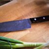 un magnifique couteau santoku posé sur une planche à découper en bois