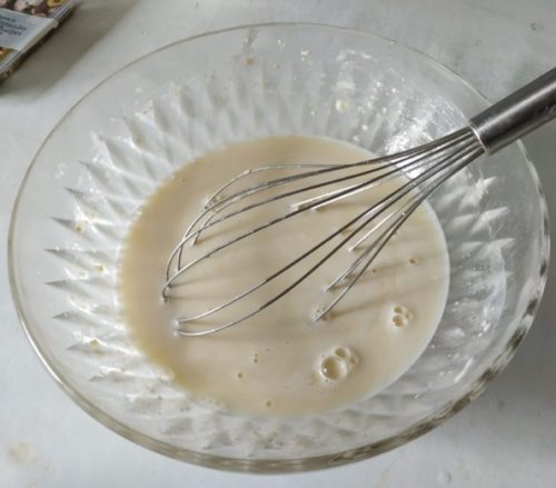Un saladier transparent en verre avec un fouet en fer et de la pâte à takoyaki